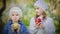 Two little girls eating red and green apples in a blooming park