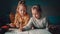 Two little girls friends or sisters of preschool age enthusiastically draw or paint a coloring book on the table by the light from