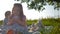 Two little girls are sitting on a picnic cover in the middle of a large green meadow