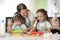 Two little girls and their beautiful mom in aprons are playing and laughing while rolling the dough in the kitchen
