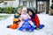 Two little kid boys and cute toddler girl sitting together on sledge. Siblings, brothers and baby sister enjoying sleigh