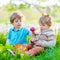 Two little kids boys and friends in Easter bunny ears during traditional egg hunt in spring garden, outdoors. Siblings