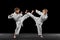 Two little kids, boys, taekwondo athletes training together isolated over dark background. Concept of sport, education