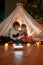 Two little kids, brother and sister using tablet pc while sitting on a blanket in a teepee made with bedsheets at home