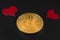 Two little red hearts over a bitcoin gold coin on black leather closeup