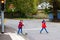 Two little schoolkids boys running and driving on scooter on autumn day. Happy children in colorful clothes and city