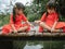 Two little sibling girls in red dress role playing fishing sitting on a wooden bridge by the pond. Childhood happiness