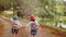 Two little sisters holding each other hands and running forward along the pine forest road on a sunny day.