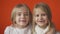 Two little toothless girls are smiling against an orange background.