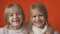 Two little toothless girls are smiling against an orange background.