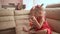 Two little twin sisters in charming red dresses are blowing soap bubbles cheerfully while sitting in the room barefoot.