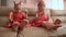 Two little twin sisters in charming red dresses are blowing soap bubbles cheerfully while sitting in the room barefoot