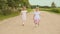 Two little twin sisters run along the road along the forest. Summer sunny day and girls in light dresses.