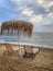 Two lounge chairs and straw parasol on the beach in Greece.