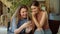 Two lovely girls are sitting on the sofa and watching something funny on the phone