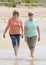 Two lovely senior mature retired women on their 60s having fun enjoying together happy walking on the beach smiling playful