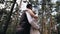 Two lovers gently hug each other standing in the middle of a beautiful pine forest.