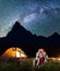 Two lovers hikers sitting together near campfire and shines camp at night under stars and looking to the starry sky
