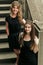Two luxury gorgeous woman  in black dress posing, standing on old stairs in city, classic gothic lady outfit