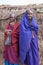 Two Maasai women stand near their house look at my camera with wondering.