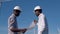 Two male African American electrical engineers stand against the backdrop of a windmill at an air power plant with a