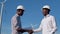 Two male African American electrical engineers stand against the backdrop of a windmill at an air power plant and shake