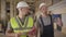 Two male Caucasian workers walking at the construction site. Adult bearded man in green vest talking to the young