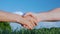 Two male farmers shake hands. Against the background of a green field and a blue sky. Deal in agribusiness concept