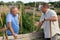 Two male farmers talking outside next to wooden fence on background with farm