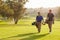 Two Male Golfers Walking Along Fairway Carrying Bags