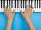 Two male hands playing on music keyboard on blue