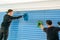 Two male professional cleaners cleaning blue blinds on a large window front with micro fiber cloths