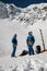 two male skiers in ski suits and helmets stand against the backdrop of a snow-covered mountain slope.