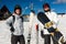 Two males in ski-suits, helmets and ski goggles standing with sn