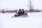 Two man on a snowmobile riding on the snow surface in the winter forest