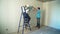 Two man workers at construction site glues wallpaper to the wall