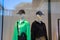 Two mannequins in a store window with one wearing a green shirt and the other wearing a black pullover sweater with a zipper