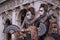 Two masks in costume, with decorated fans, standing in front of the arches at St Marks Square during the Venice Carnival