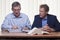 Two mature businessmen or partners discussing a project sitting at a desk with folder and book