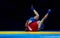 Two men in blue and red sambo wrestling on a yellow wrestling carpet in the gym