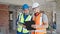 Two men builders reading document using touchpad shake hands at construction site