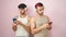 Two men couple using smartphones and headphones with relaxed expression over isolated pink background