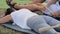 Two men doing massage for woman with bamboo sticks at outdoor yoga festival