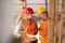 Two men dressed in shirts, orange work vests and helmets explore construction documentation on the building site near