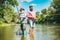 Two men friends fishing. Flyfishing angler makes cast, standing in river water. Old and young fisherman.