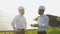 Two men in hard helmets discussing project at solar farm. Male engineers with scrolls of engineering drawing