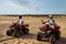 Two men in helmets ride on atv in desert