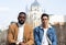 Two men posing serious sitting. Afro-american and caucasian man. Almudena cathedral in the background. Madrid. Spain