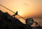 Two Men Pulling and Pushing Uphill A Big Rock Together With a Metal Chain In Front Of Beach Sunrise