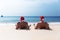 Two men in Santa Claus red hat sit on the beach in morning hangover Christmas holiday party dreams